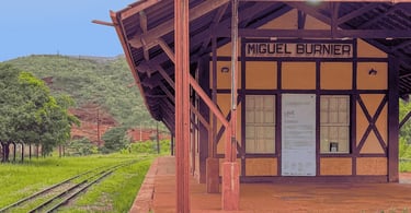 Antiga estação ferroviária amarela e marrom com placa de Miguel Burnier e trilhos cercados por grama