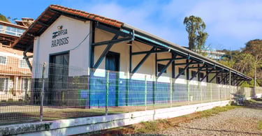Estação ferroviária de Raposos com fachada branca e azul preservada em cenário urbano de Minas Gerai