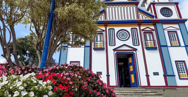 Igreja Matriz de Datas, em Minas Gerais, com fachada colorida, jardim florido e árvores ao redor