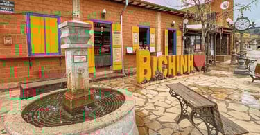 Praça em Bichinho MG com chafariz de pedra, letreiro turístico, casarões coloridos e relógio de rua