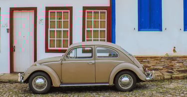 Fusca bege estacionado em rua de pedra com casarão histórico ao fundo em Ouro Preto, MG