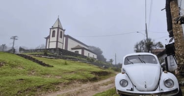 Fusca branco diante da Igreja Matriz de Conceição do Ibitipoca em manhã de neblina