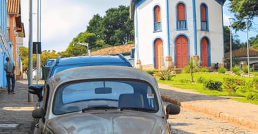 Fusca antigo em rua de pedra de Santa Bárbara MG com igreja histórica e jardim ao fundo