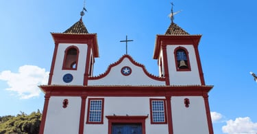 Igreja Matriz de Sabará MG com fachada branca e detalhes vermelhos sob céu azul
