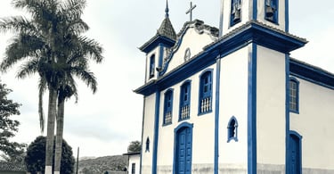 Igreja de Nossa Senhora do Rosário em Cocais, MG, com fachada branca e azul ao lado de palmeira