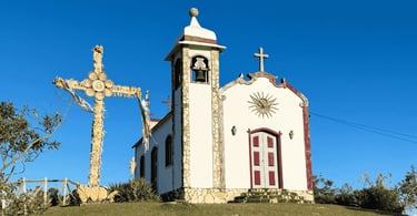 Igreja no Morro Redondo em Ipoema MG com cruzeiro ornamentado, torre com sino e céu azul