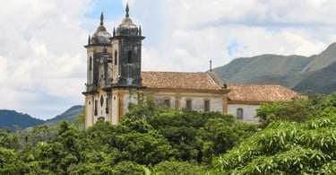 Igreja histórica em Ouro Preto cercada por vegetação, montanhas e paisagem colonial mineira ao fundo