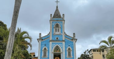 Igreja de Lagoa Dourada com cores azuis, céu nublado e coqueiros em volta