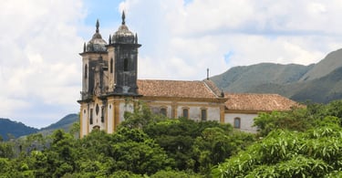 Igreja histórica em Ouro Preto MG cercada por vegetação verde e montanhas ao fundo