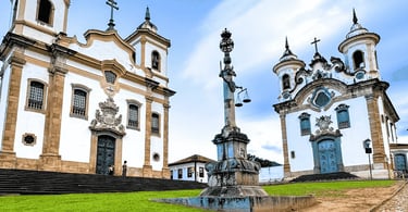 Praça Minas Gerais em Mariana, MG, com pelourinho ao centro e igrejas históricas em lados opostos