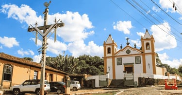 Igreja histórica de Bichinho MG com cruzeiro artesanal, casario colonial e céu azul com nuvens