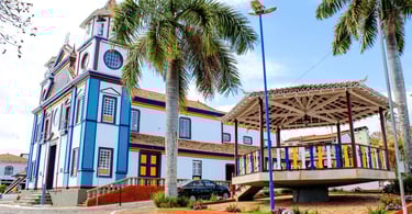 Igreja Matriz e coreto na praça de Datas MG com arquitetura colonial, palmeiras e praça com cores