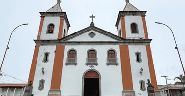 Igreja histórica branca com detalhes verticais laranjas e bustos na entrada em Lagoa Dourada