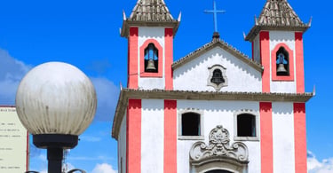 Igreja Matriz de Lavras Novas com fachada branca e rosa, torres coloniais e céu azul
