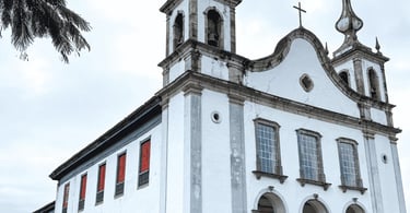 Igreja Matriz de Catas Altas MG com fachada colonial branca, janelas vermelhas e torres sineiras