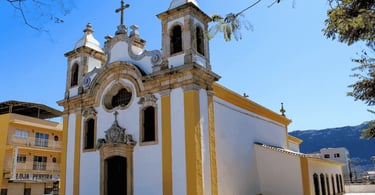 Igreja Matriz de Ouro Branco MG com fachada branca e amarela, torres coloniais e montanhas