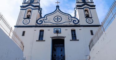 Igreja Matriz de Raposos, em Minas Gerais, com fachada branca e detalhes azuis vista de baixo