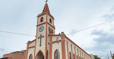 Igreja Matriz de Santa Cruz de Minas com torre alta, relógio na fachada e detalhes em tom rosado