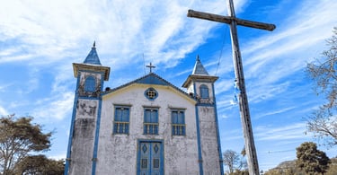Igreja histórica em São Gonçalo do Rio das Pedras com fachada branca, detalhes azuis e grande cruz