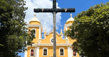 Igreja Matriz de São Thomé das Letras com fachada amarela, cruzeiro e árvores ao redor