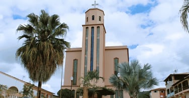 Igreja Matriz de Morro do Pilar sob céu nublado, emoldurada por palmeiras