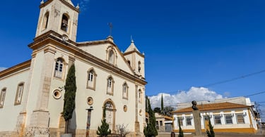Igreja Matriz de Nazareno ao lado de casarão colonial e monumento na praça central
