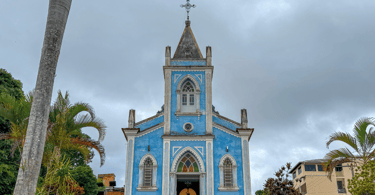 Igreja de Lagoa Dourada com cores azuis, céu nublado e coqueiros em volta