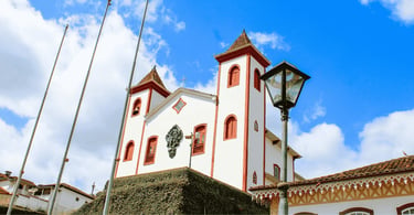 Igreja Nossa Senhora do Carmo em Serro MG com fachada branca, detalhes vermelhos e céu azul