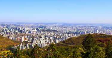 Vista de um mirante da cidade de Belo Horizonte, com prédios, casas, montanhas e um céu aberto