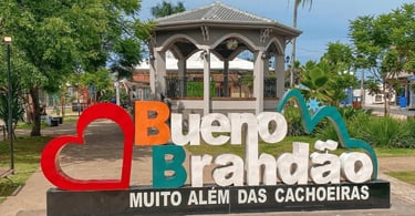 Letreiro turístico de Bueno Brandão MG em praça arborizada com coreto e jardins ao fundo