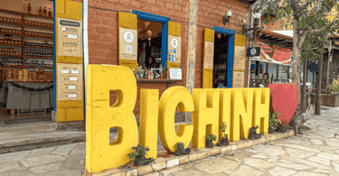 Letreiro amarelo de Bichinho com um coracao e uma loja de produtos da regiao ao fundo