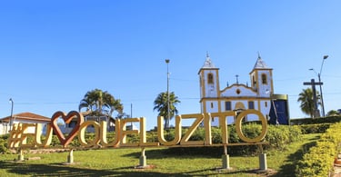 Letreiro Eu Amo Queluzito na praça central com igreja matriz ao fundo em Minas Gerais