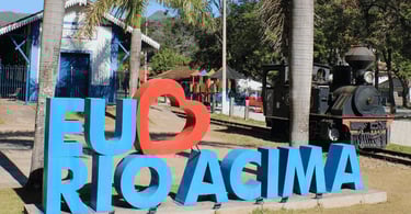 Letreiro Eu amo Rio Acima com locomotiva histórica, estação ferroviária e palmeiras, área turística