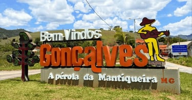 Letreiro de boas-vindas em Gonçalves MG com paisagem da Mantiqueira, céu azul e morros ao fundo