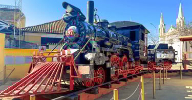 Locomotiva antiga em exposição em Diamantina, MG, com rodas vermelhas e igreja ao fundo