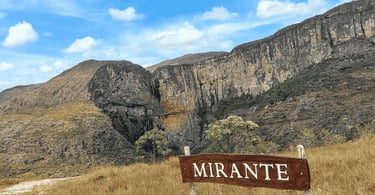 Mirante da Cachoeira do Tabuleiro com paredão rochoso, campo aberto e céu azul com nuvens