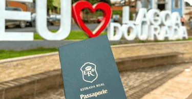 Capa verde do Passaporte da Estrada Real em frente ao letreiro Eu Amo Lagoa Dourada