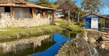 Cachoeira do Comércio em São Gonçalo do Rio das Pedras MG com pequeno curso d’água, casas rústicas