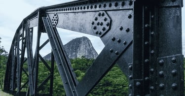 Pontilhão de Ferro, com a Pedra que é ponto turistico da cidade ao fundo e árvores, em Ladainha MG