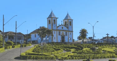 Igreja histórica em Queluzito com jardim bem cuidado, palmeiras e céu azul ao fundo