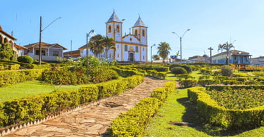 aminho de pedra em praça arborizada com a Igreja Matriz ao fundo. Queluzito, MG