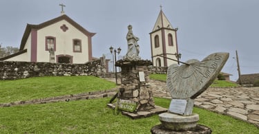 Igreja de Ibitipoca em área elevada, com fachada clara, torre, gramado e monumentos de pedra