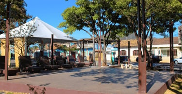 Praça arborizada com bancos, cobertura e casarões antigos em Honório Bicalho, distrito de Nova Lima
