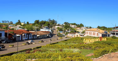 Vista panorâmica de Queluzito com praça ajardinada, letreiro turístico e casas ao redor