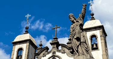 Estátua de pedra do profeta Daniel com braço erguido contra o céu azul, torres da igreja, Congonhas