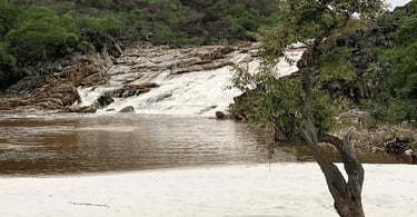 Queda d’água da Cachoeira do Telésforo com rio, areia clara e vegetação ao redor