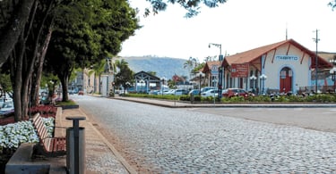 Rua em Itabirito com calçamento de pedra, estação ferroviária, bancos e árvores na praça central