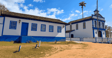 Estrada de terra, casa histórica e igreja historica, com cores branca e azul, na Vila do Biribiri