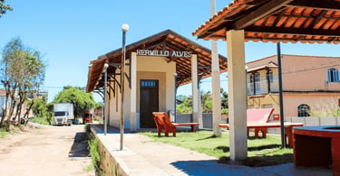 Antiga estação ferroviária de Hermílio Alves com plataforma coberta, bancos e construções ao redor
