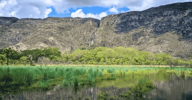 Lagoa com vegetação verde e paredão rochoso na Serra do Cipó